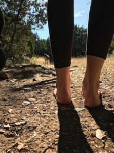 woman walking barefoot in woods practicing graounding